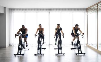 Four people are riding stationary bikes 
